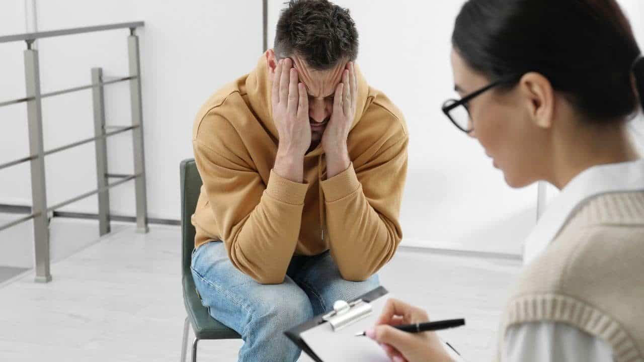 a man sitting in a chair holding his head with both hands