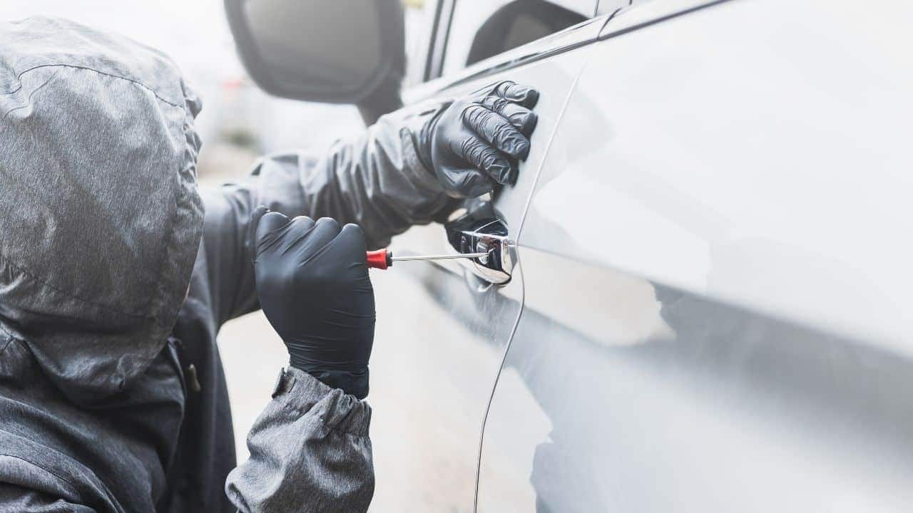 a person wearing black gloves and holding a screwdriver to a car door