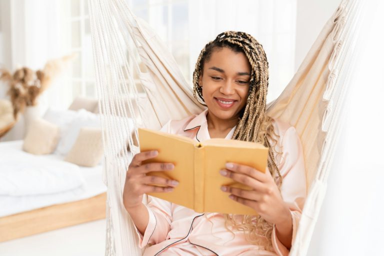 Serene pretty young afro woman reading a book, novel in pajamas, studying